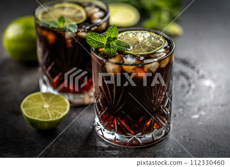 Tropical alcoholic cocktail Cuba Libre composed of white rum, cola, ice cubes, lime and mint 112330460
