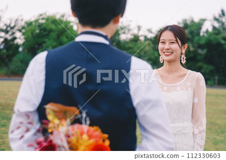 Groom hiding the bouquet he gives to the bride behind his back 112330603