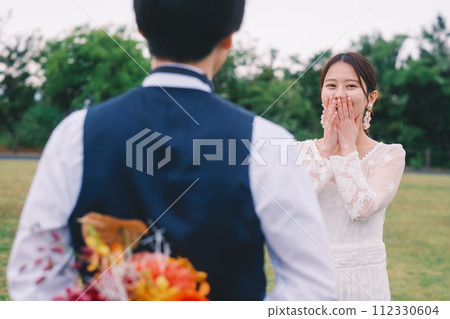 Groom hiding the bouquet he gives to the bride behind his back Groom hiding the bouquet he gives to the bride behind his back 112330604