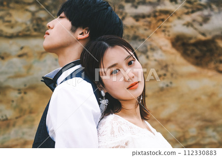 Bride and groom standing back to back on a rock 112330883