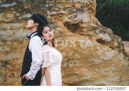 Bride and groom standing back to back on a rock 112330887