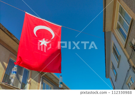 Turkey's national red flag, a white five-pointed star with a crescent moon, hung out into street, stretched between high-rise buildings with hanging water bottles. Preparation for a national wedding 112330988