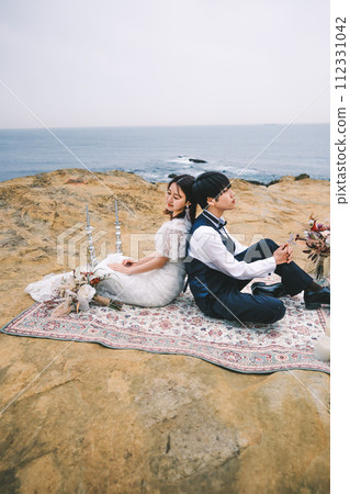 bride and groom sitting back to back on the beach 112331042