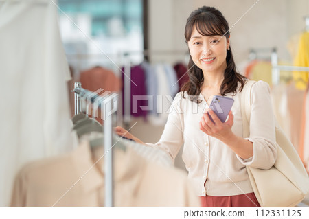 A middle-aged woman operating a smartphone while shopping at a store 112331125