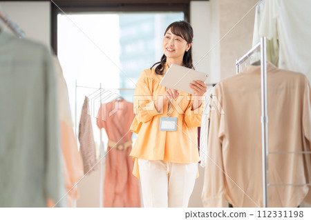 A middle-aged female clerk working while operating a tablet in an apparel shop 112331198