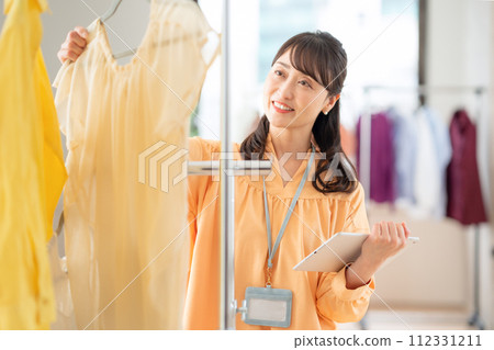 A middle-aged female clerk working while operating a tablet in an apparel shop 112331211