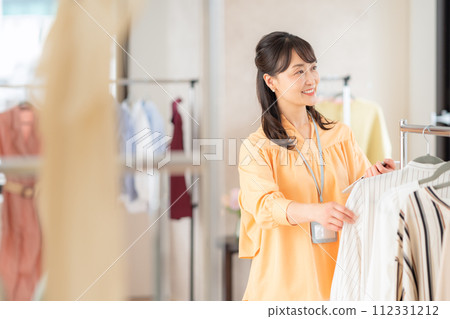一位中年女店員在一家服裝店邊操作平板電腦邊工作 一位中年女店員在一家服裝店邊操作平板電腦邊工作 112331212