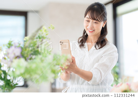 一位中年婦女在客廳用智能手機拍攝她愛好的花藝 112331244
