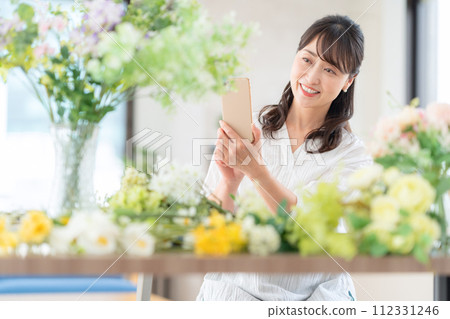 A middle-aged woman who shoots her hobby flower arrangement with a smartphone in the living room A middle-aged woman who shoots her hobby flower arrangement with a smartphone in the living room 112331246