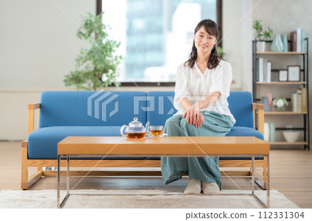 Middle-aged woman drinking tea in the living room Middle-aged woman drinking tea in the living room 112331304