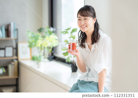 Middle-aged woman drinking tomato juice in the living room 112331351
