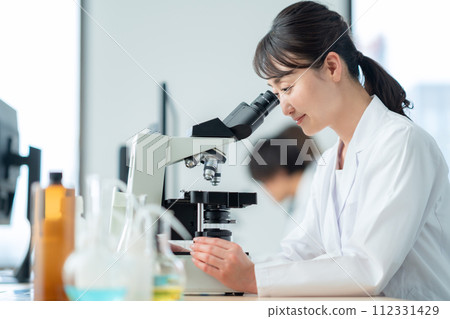 A middle-aged woman looking into a microscope for research and experiments A middle-aged woman looking into a microscope for research and experiments 112331429