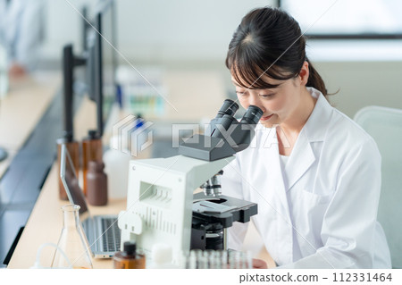 A middle-aged woman looking into a microscope for research and experiments 112331464