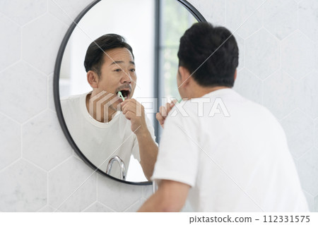 A man in his 50s brushing his teeth 112331575