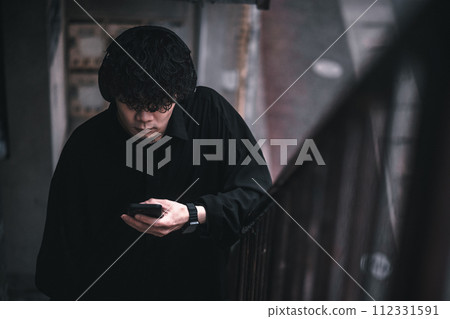 A man listening to music on his smartphone on the stairs of an old building A man listening to music on his smartphone on the stairs of an old building 112331591