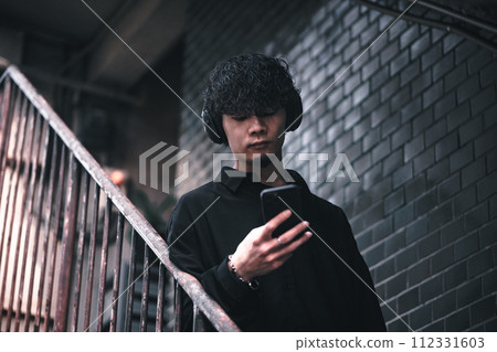 A man listening to music on his smartphone on the stairs of an old building A man listening to music on his smartphone on the stairs of an old building 112331603