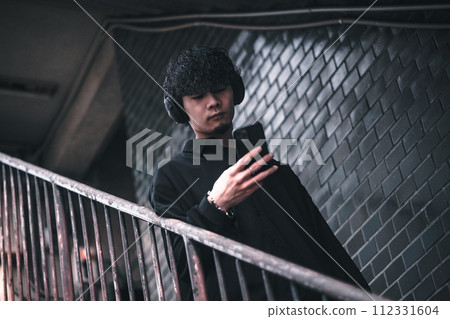 A man listening to music on his smartphone on the stairs of an old building A man listening to music on his smartphone on the stairs of an old building 112331604