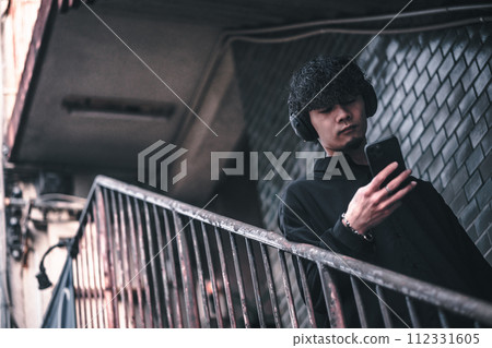 A man listening to music on his smartphone on the stairs of an old building A man listening to music on his smartphone on the stairs of an old building 112331605