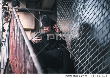 A man listening to music on his smartphone on the stairs of an old building 112331621