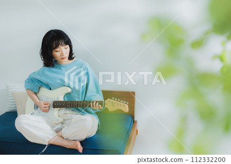 woman playing guitar in living room 112332200
