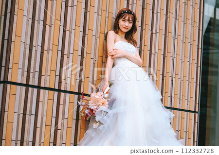 Bride in a wedding dress standing with a bouquet in front of a colorful wall Bride in a wedding dress standing with a bouquet in front of a colorful wall 112332728