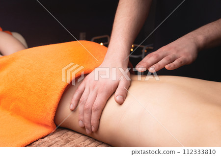 Side view in shallow depth of field. Massage of the lower back by a male masseur. Volumetric light. Live photography 112333810