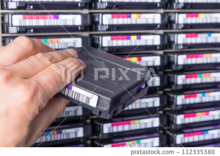 hand of a technician holding data storage magnetic tape in front of data storage array 112335380