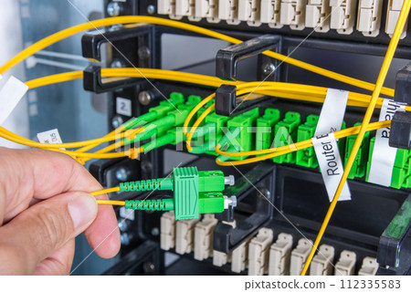 Hand of computer technician connecting fiber optics cable into data switch Hand of computer technician connecting fiber optics cable into data switch 112335583