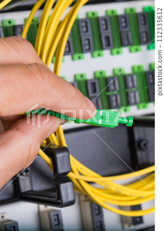 closeup of hand of administrator connecting network cable into switch 112335612