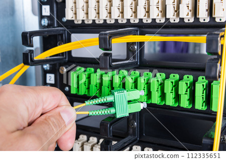 Hand of computer technician connecting fiber optics cable into data switch Hand of computer technician connecting fiber optics cable into data switch 112335651