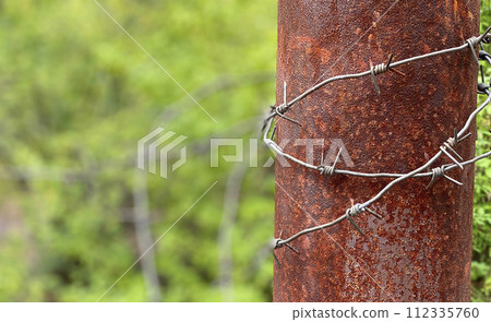 Close-up of a rusty metal pole with barbed wire wrapped around it 112335760