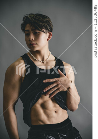年輕人捲起他的背心來展示他的腹肌 年輕人捲起他的背心來展示他的腹肌 112336498