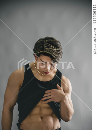 Young man rolling up his tank top to show his abs Young man rolling up his tank top to show his abs 112336511