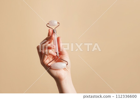 Jade roller gua sha in woman hand on pastel beige background with copy space. natural products for skin care Jade roller gua sha in woman hand on pastel beige background with copy space. natural products for skin care 112336600
