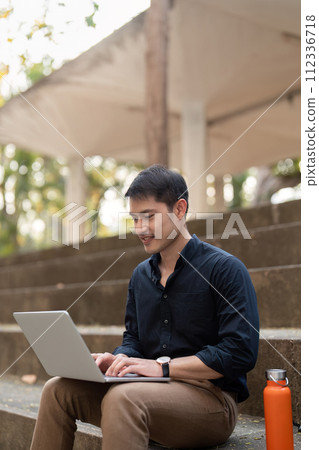 Asian businessman with reusable eco friendly ecological cup using laptop and sitting outside the office building. Eco friendly, sustainable lifestyle concept Asian businessman with reusable eco friendly ecological cup using laptop and sitting outside the office building. Eco friendly, sustainable lifestyle concept 112336718