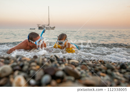 Young man with his son 4 years old swim near shore in masks with snorkels sunset, background yacht. Young man with his son 4 years old swim near shore in masks with snorkels sunset, background yacht. 112338005