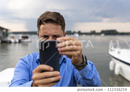 Man holding smartphone in his hands at river and taking photographs Man holding smartphone in his hands at river and taking photographs 112338259