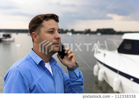 Man talking on the phone beside luxury yacht at port. Nautical and marine concept Man talking on the phone beside luxury yacht at port. Nautical and marine concept 112338338
