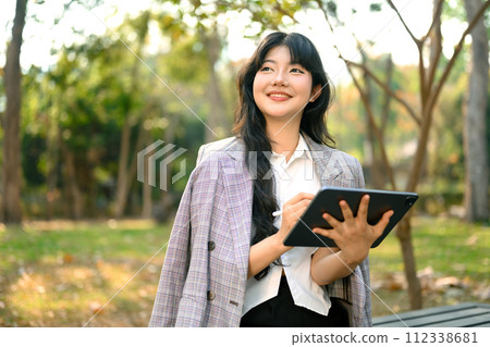 Shot of confident businesswoman holding digital tablet and looking away sitting in park Shot of confident businesswoman holding digital tablet and looking away sitting in park 112338681