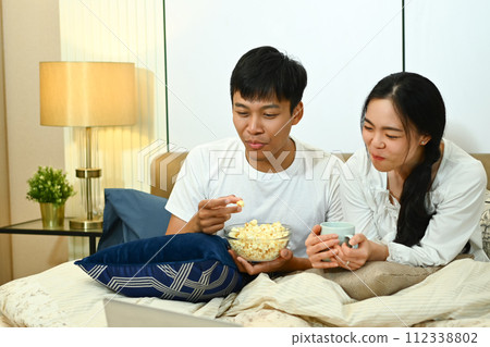 Happy marriage couple watching TV and eating popcorn on couch at home Happy marriage couple watching TV and eating popcorn on couch at home 112338802