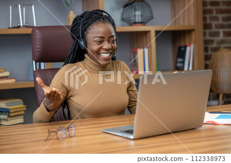 Woman with dreadlocks in headphones works remotely as a tech streamer using laptop 112338973