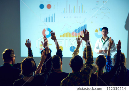 Interactive business workshop with participants engaging with presenter, business coach in front of graphical data analysis. Interactive business workshop with participants engaging with presenter, business coach in front of graphical data analysis. 112339214