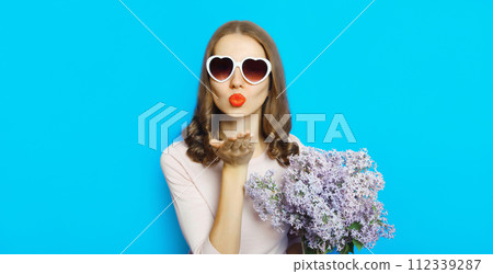 Portrait of beautiful happy young woman blowing kiss with bouquet of flowers Portrait of beautiful happy young woman blowing kiss with bouquet of flowers 112339287