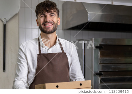 Man holding pizza boxes serves as a dedicated worker in the restaurant's fast food kitchen Man holding pizza boxes serves as a dedicated worker in the restaurant's fast food kitchen 112339415