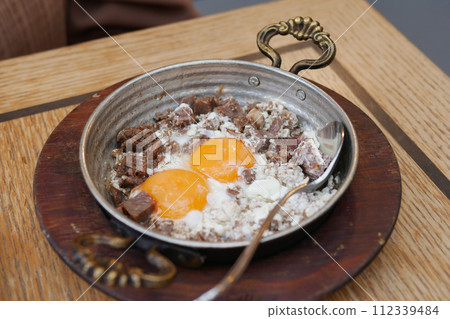 Turkish scrambled eggs with roasted meat in copper pan 112339484