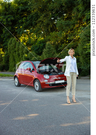 Businesswoman raises her finger while standing on country road needs help with her broken car Businesswoman raises her finger while standing on country road needs help with her broken car 112339631