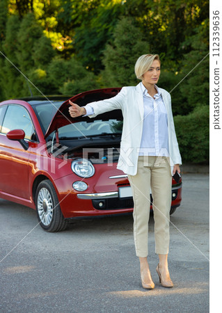 Woman standing near their broken car and hitchhiking having problems with her auto Woman standing near their broken car and hitchhiking having problems with her auto 112339636