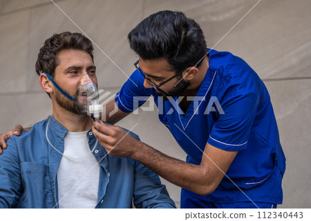 Male nurse putting an oxygen mask on a patient in wheelchair 112340443