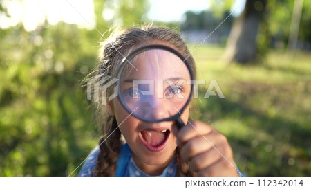 the girl holds a magnifying glass in her hands. gaining knowledge and curiosity concept. a schoolgirl girl with a black magnifying glass is examining lifestyle something, park on the background 112342014