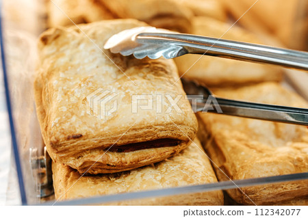 puff pastry in a pastry shop. puff pastry bun. pie with sweet filling. pastry tongs puff pastry in a pastry shop. puff pastry bun. pie with sweet filling. pastry tongs 112342077